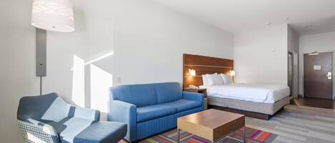 A hotel room with a bed, a blue sofa, a small table, a chair, and a colorful rug.