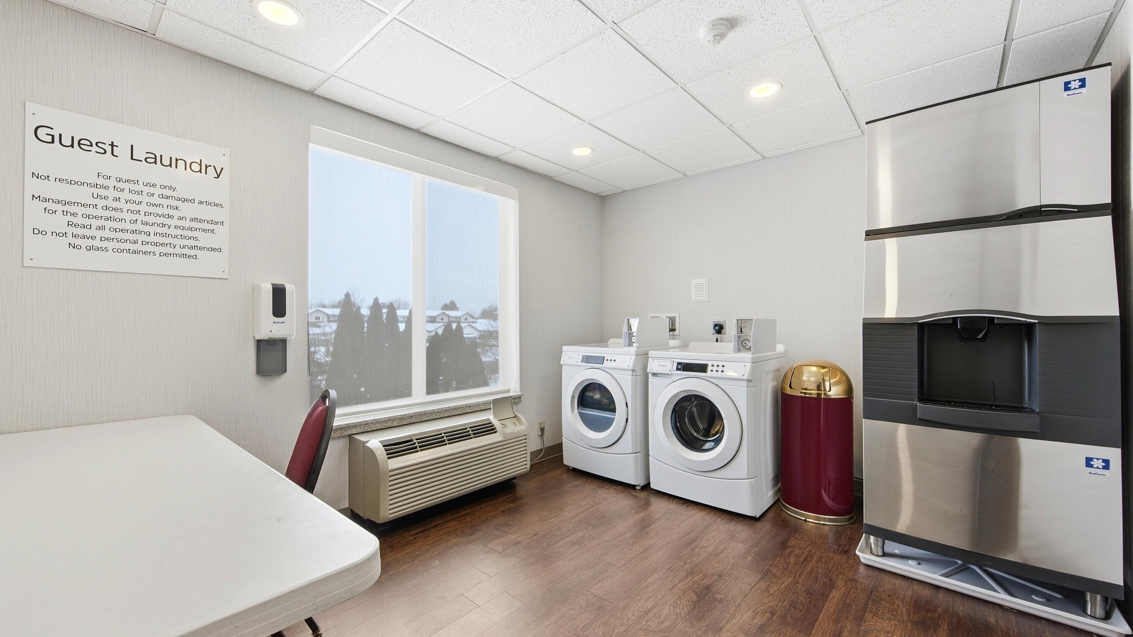 A guest laundry area with two washing machines, a dryer, a refrigerator, and a window with a view of houses.