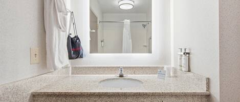 A bathroom with a granite countertop, a sink, a mirror, a towel rack, a hair dryer bag, and toiletries.