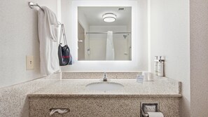 A bathroom with a granite countertop, a sink, a mirror, a towel rack, a hair dryer bag, and toiletries.