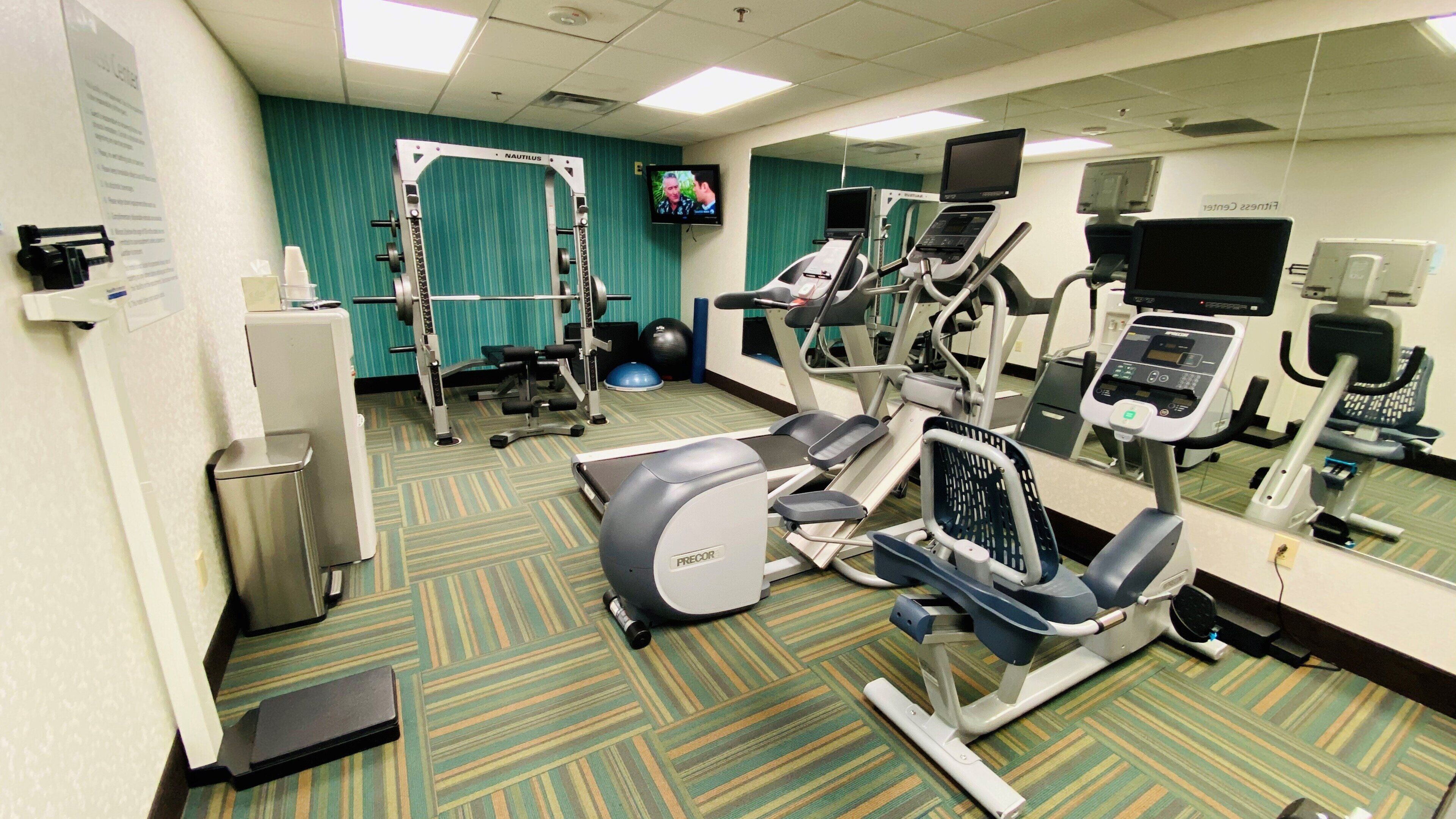 A gym with exercise equipment, a television, and a mirrored wall.