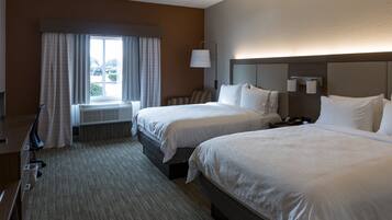 A hotel room with two beds, a desk, a chair, a window with curtains, and a lamp.