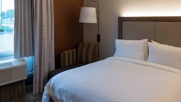 Une chambre d’hôtel avec un lit, une lampe de chevet, une fenêtre avec des rideaux et un climatiseur fixé au mur.