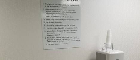 A fitness center sign with rules, a water dispenser, and a trash bin.