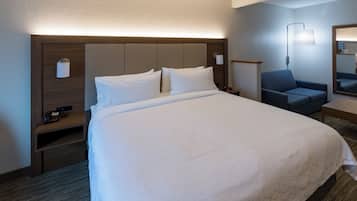 A hotel room with a large bed, a bedside table with a lamp, a chair, and a mirror.
