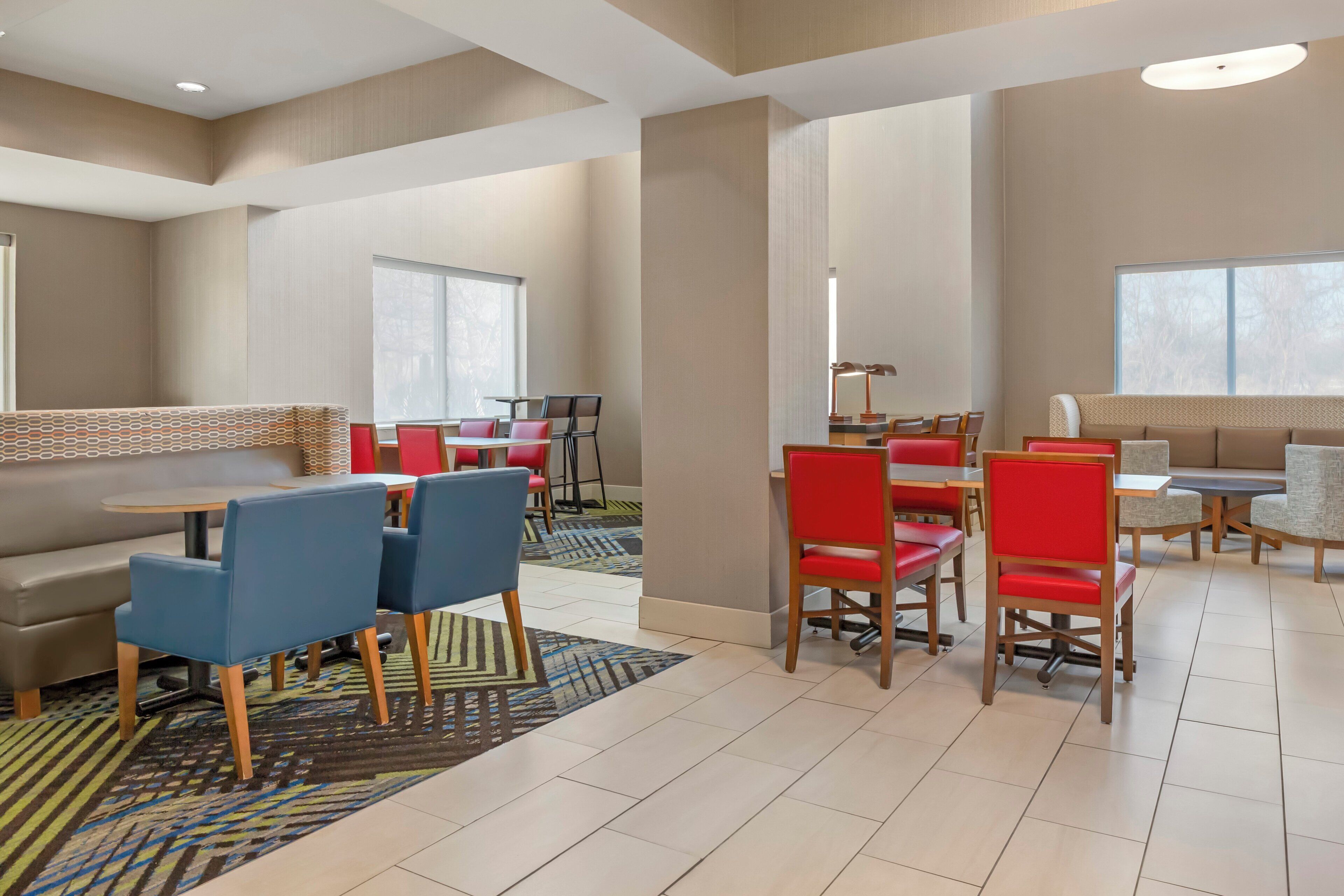 A modern hotel lobby with a seating area featuring blue and red chairs, a sofa, and a patterned rug.