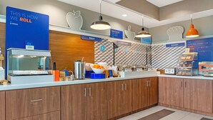 A modern kitchen with wooden cabinets, a fruit display, and a sign indicating the bread and pastry section. - Holiday Inn Express Hotel & Suites Hillview by IHG (Louisville)