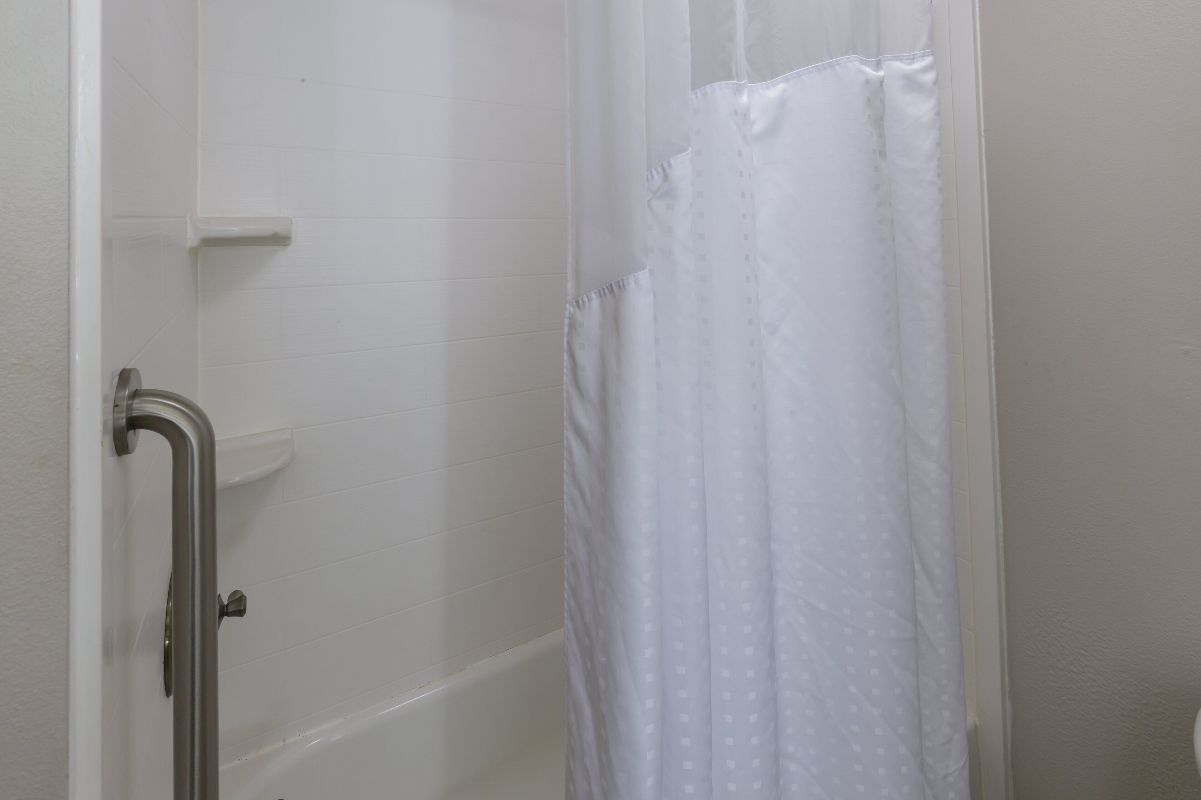 A bathroom with white tiled walls, a white shower curtain, and a grab bar.