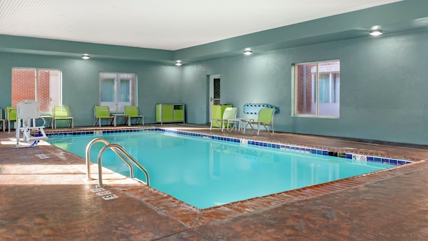Ein Hallenbad mit klarem Wasser, umgeben von grünen Stühlen und einem gefliesten Boden.