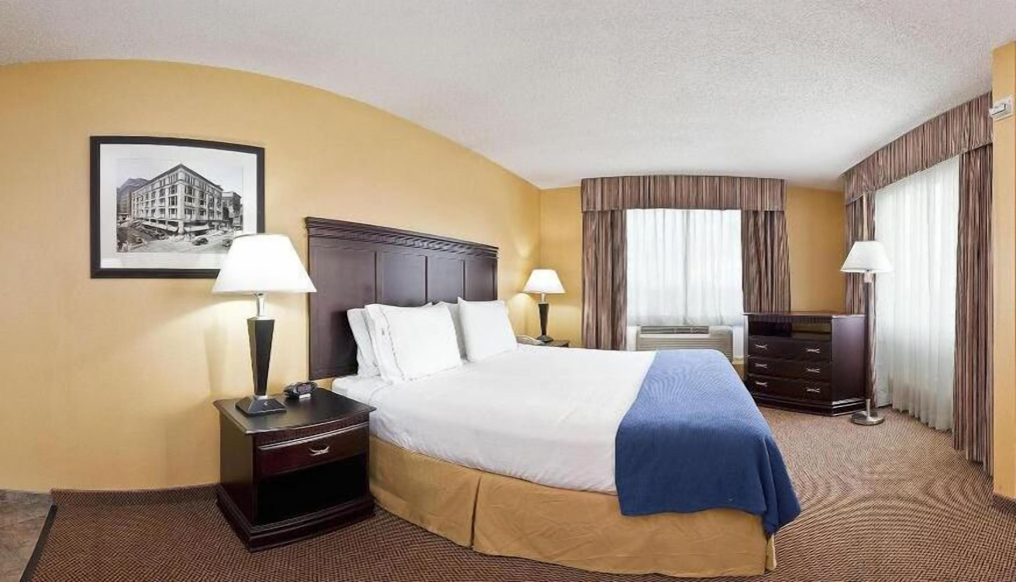A hotel room with a large bed, two bedside tables with lamps, a desk with a chair, and a picture of a building on the wall.