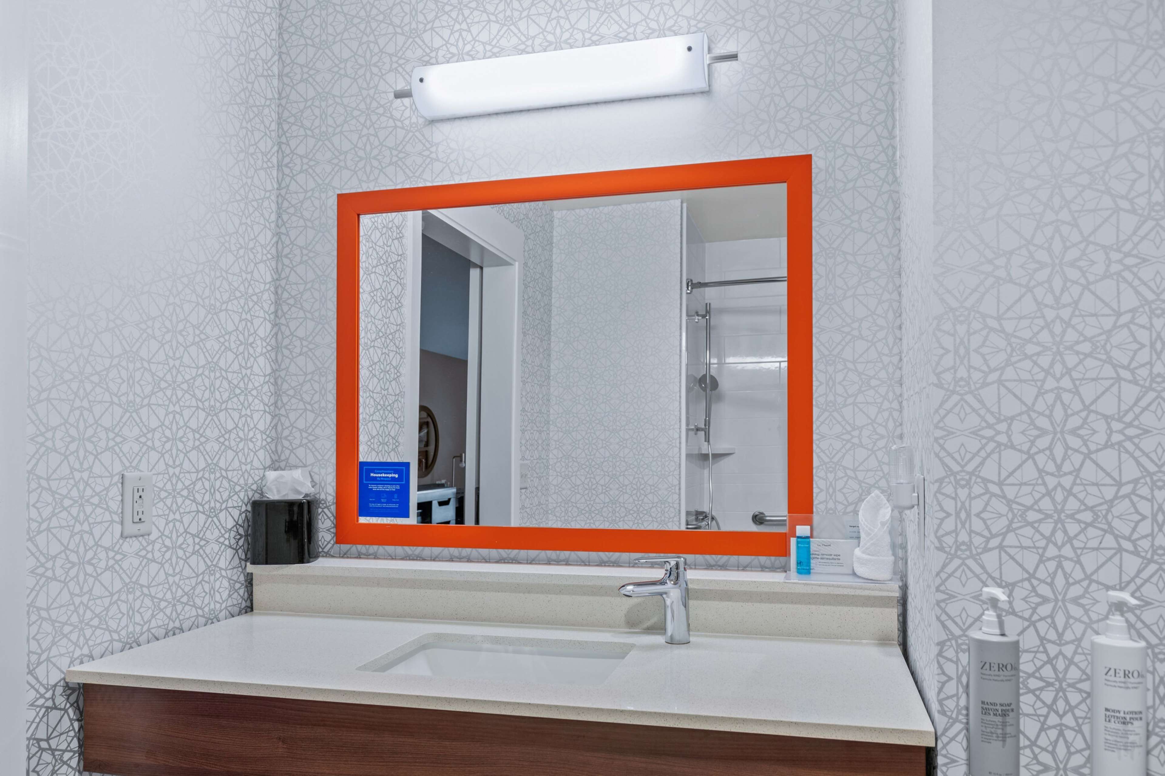 Ein Badezimmer mit einem weißen Waschbecken, einem Spiegel mit orangefarbenem Rahmen und Wandverkleidungen mit Muster.