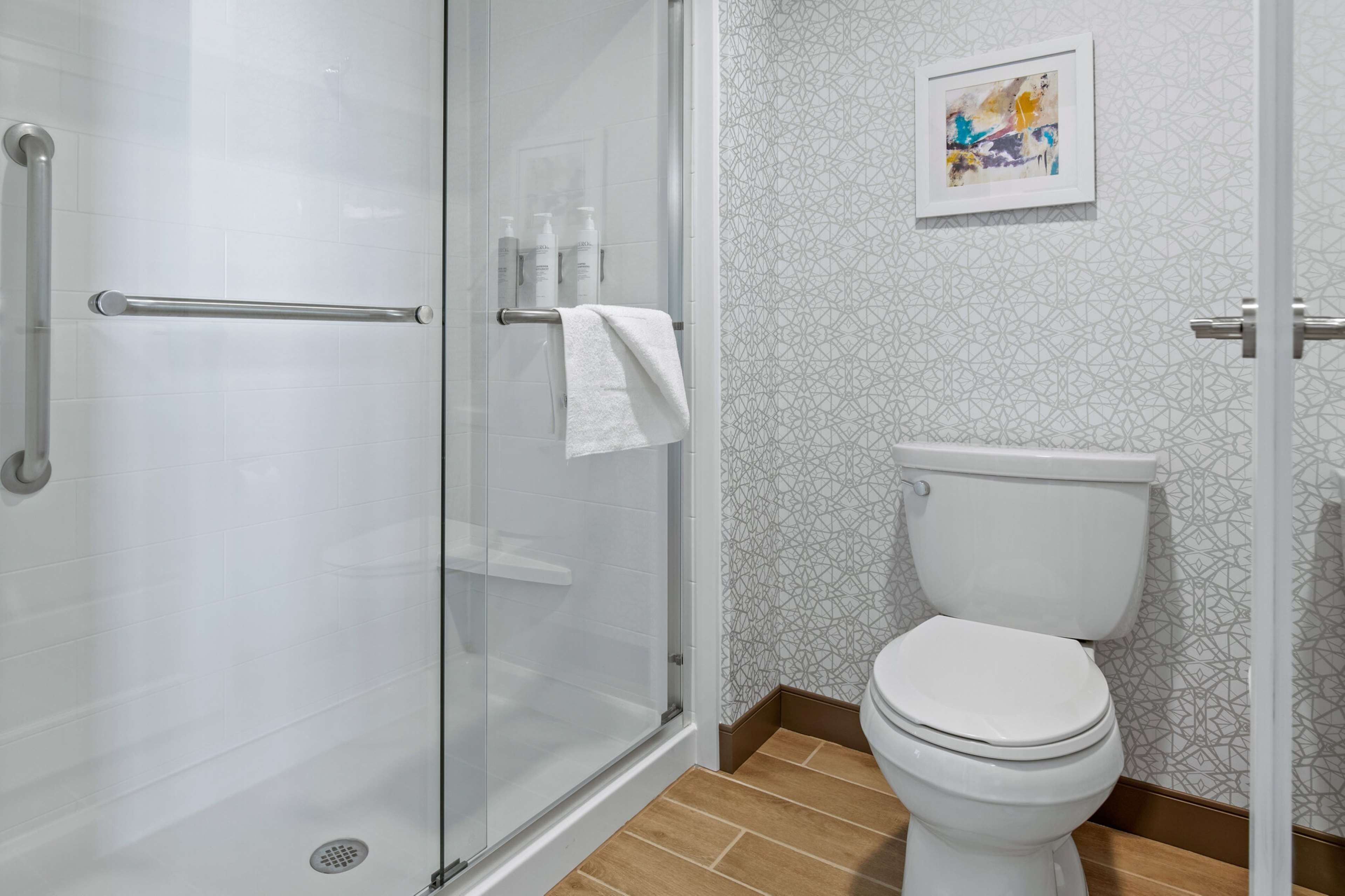 Un baño con cabina de ducha de vidrio, inodoro blanco y pared con diseño.