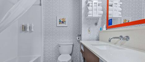 A modern bathroom with a bathtub, toilet, and vanity with a large mirror.