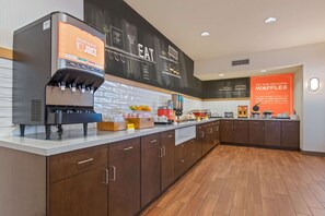 A modern kitchen with a juice dispenser, a chalkboard menu, and a sign promoting waffles.