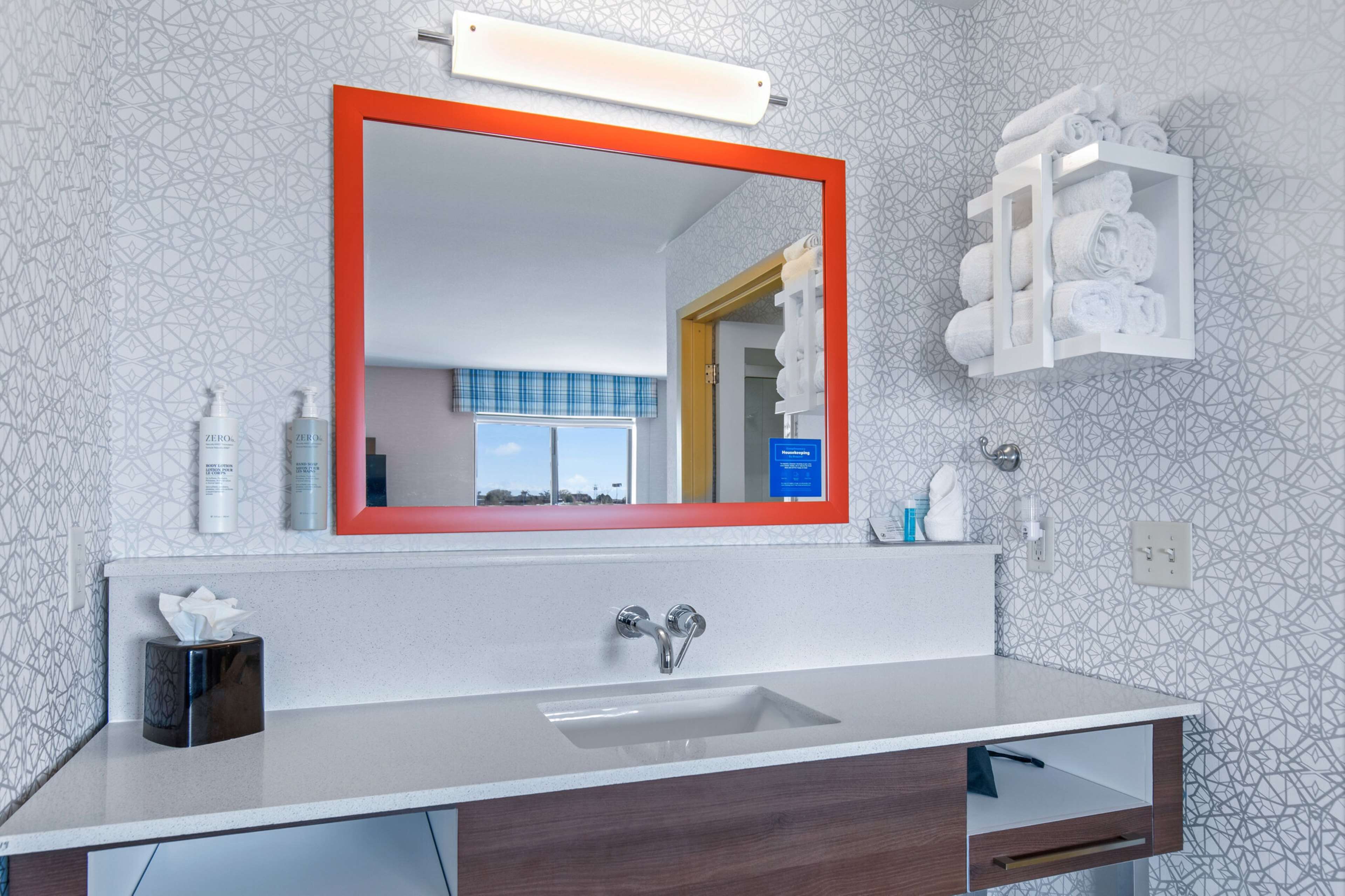 A modern bathroom with a large mirror, white countertop, and a towel rack.