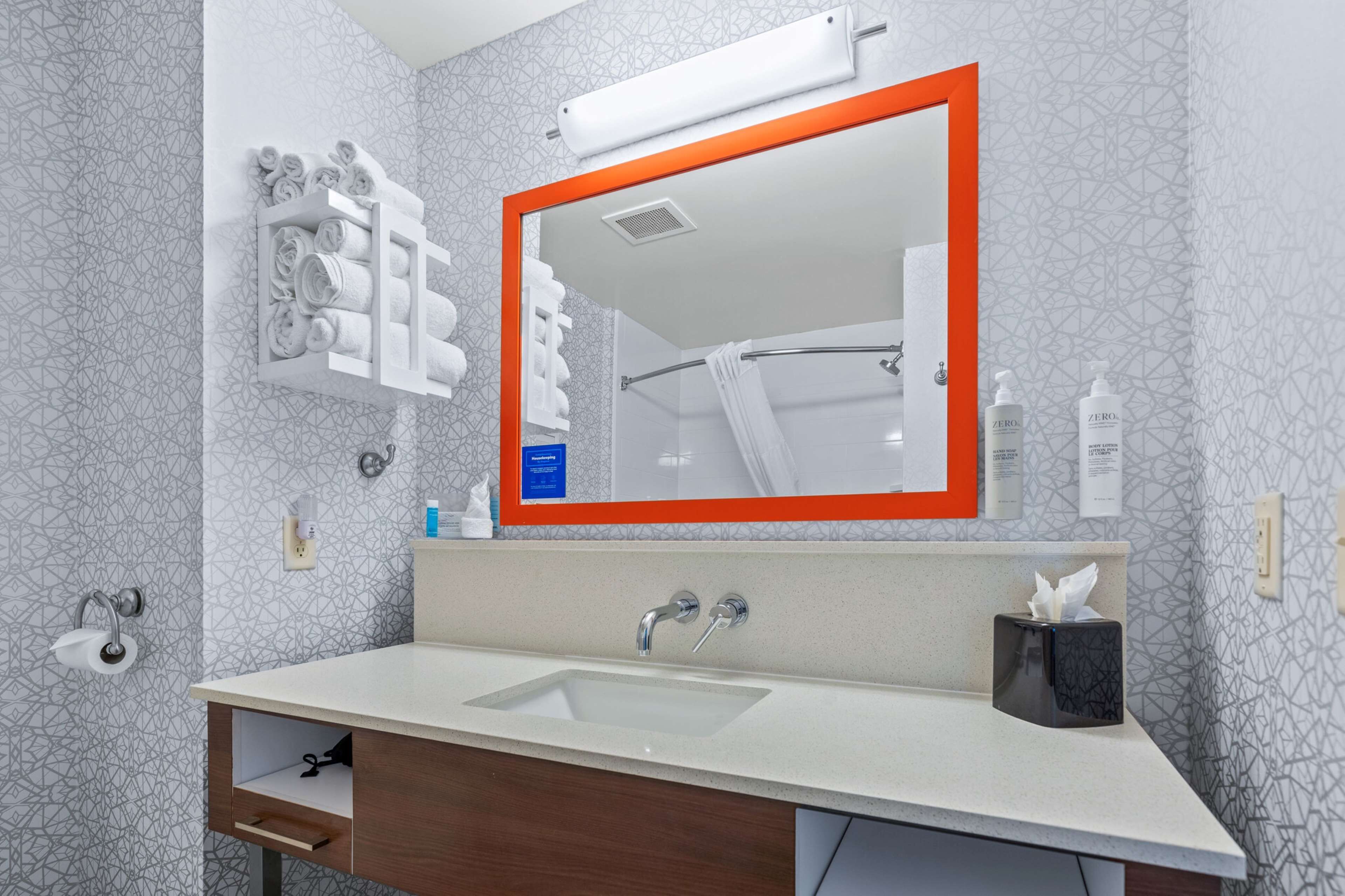 Une salle de bain moderne avec un grand miroir, un porte-serviettes, un lavabo et un sèche-mains.