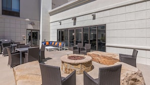 An outdoor patio area with wicker furniture, a stone fire pit, and a view of a building with large windows. - Hampton Inn & Suites Greeley (Greeley)