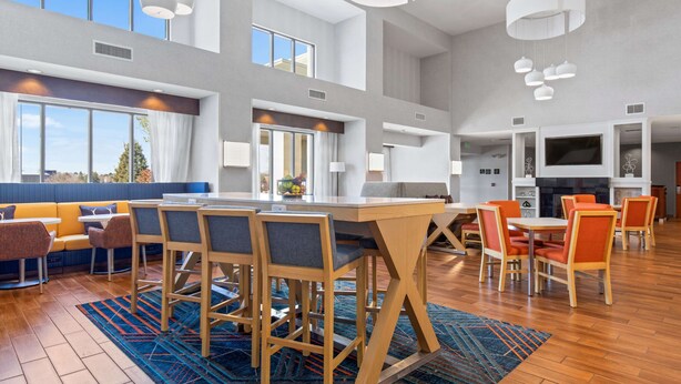 A spacious dining area with a long table and multiple chairs, a seating area with sofas and a bar, and large windows providing natural light. - Hampton Inn & Suites Greeley (Greeley)
