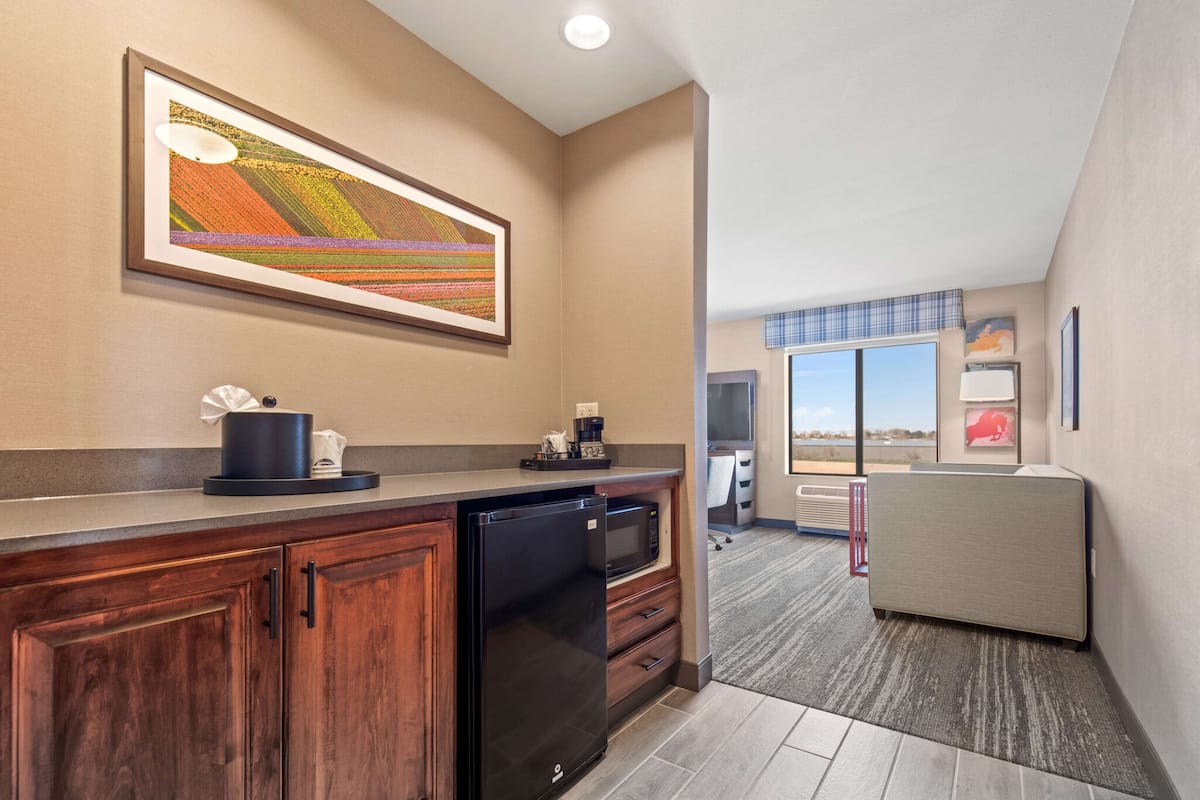 A modern kitchen with a built-in dishwasher, microwave, and coffee maker. There is a large framed artwork on the wall, a window with a view, and a seating area with a view.