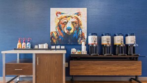 A kitchenette with a coffee station, a painting of a bear, and a wooden cabinet.