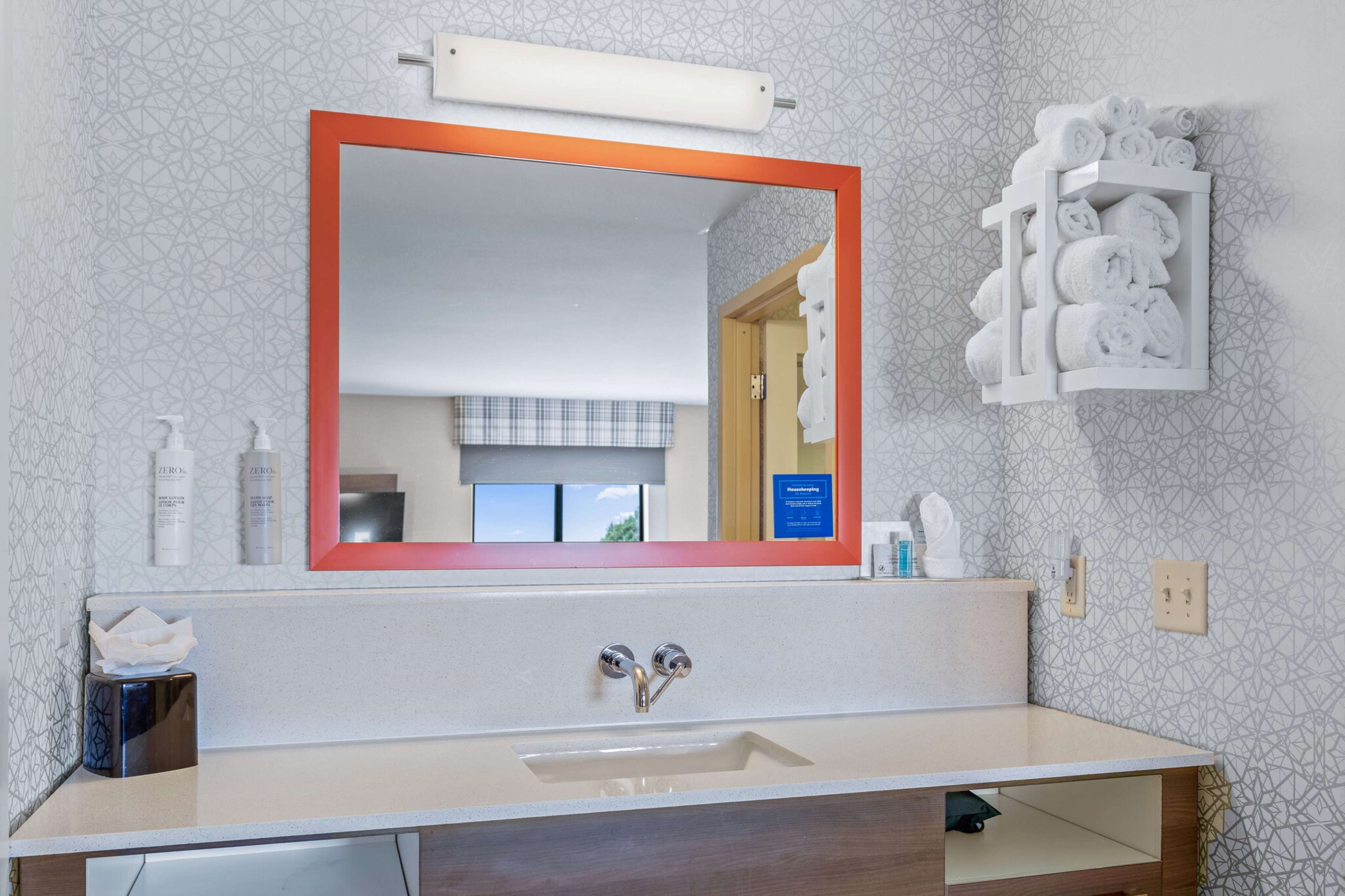 Un baño con un espejo grande, un lavabo y un perchero para toallas.