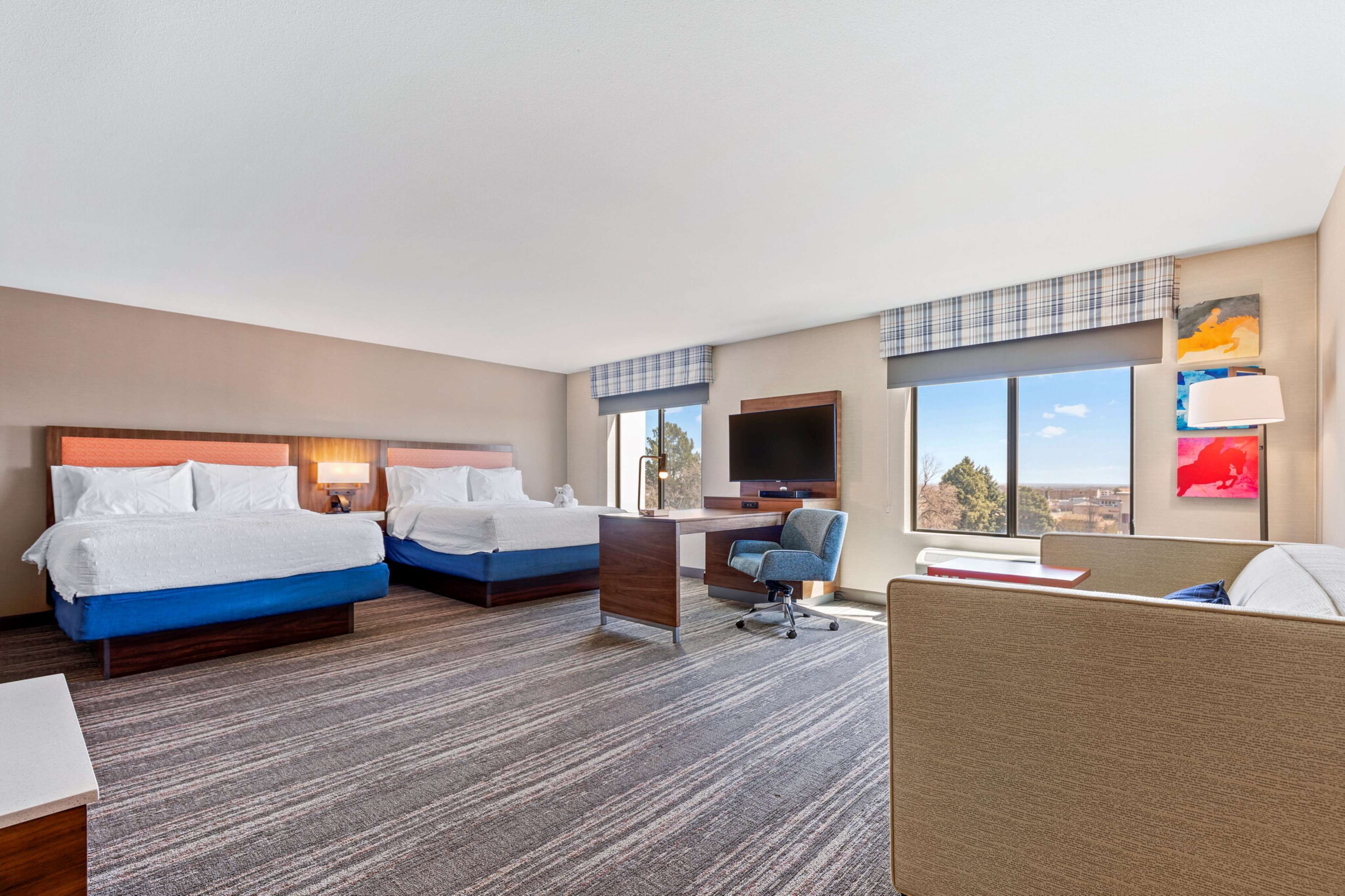 A hotel room with two beds, a desk, a chair, and a view of the city.