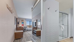 A modern hotel room with a glass shower enclosure, a desk with a chair, and a view of the outdoors. - Hampton Inn & Suites Greeley (Greeley)