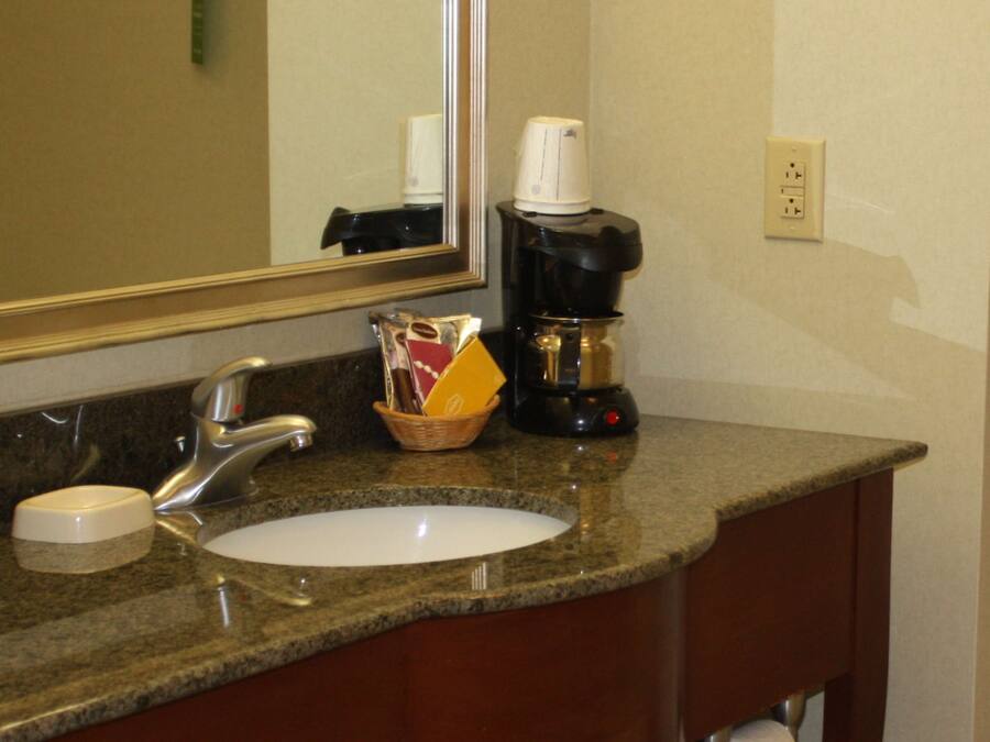 A bathroom with a sink, mirror, coffee maker, and toiletries.