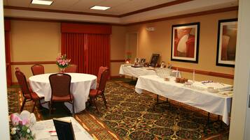 Un salón de conferencias con mesas redondas, sillas, una cortina roja, obras de arte enmarcadas y una mesa de buffet con comida y bebidas.