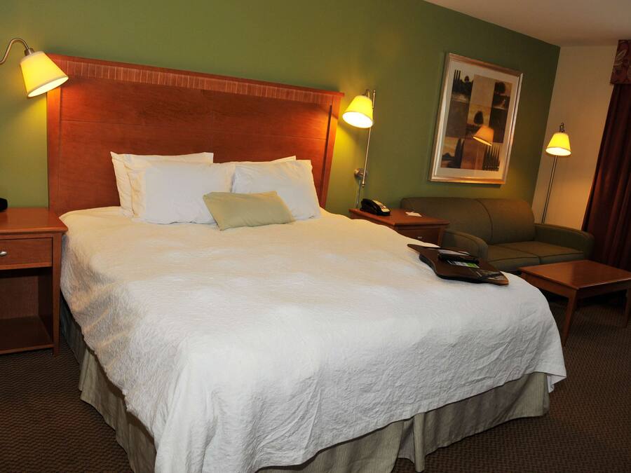 A hotel room with a large bed, two bedside tables, a nightstand, a chair, a small table, and a painting on the wall.