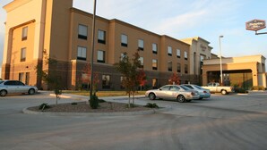 A Hampton Inn hotel with a parking lot, a few cars, and a clear sky.