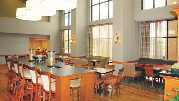 A spacious dining area with wooden tables and chairs, large windows, and a ceiling fan.