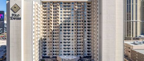 Um edifício alto com várias varandas, uma entrada central e área de estacionamento.