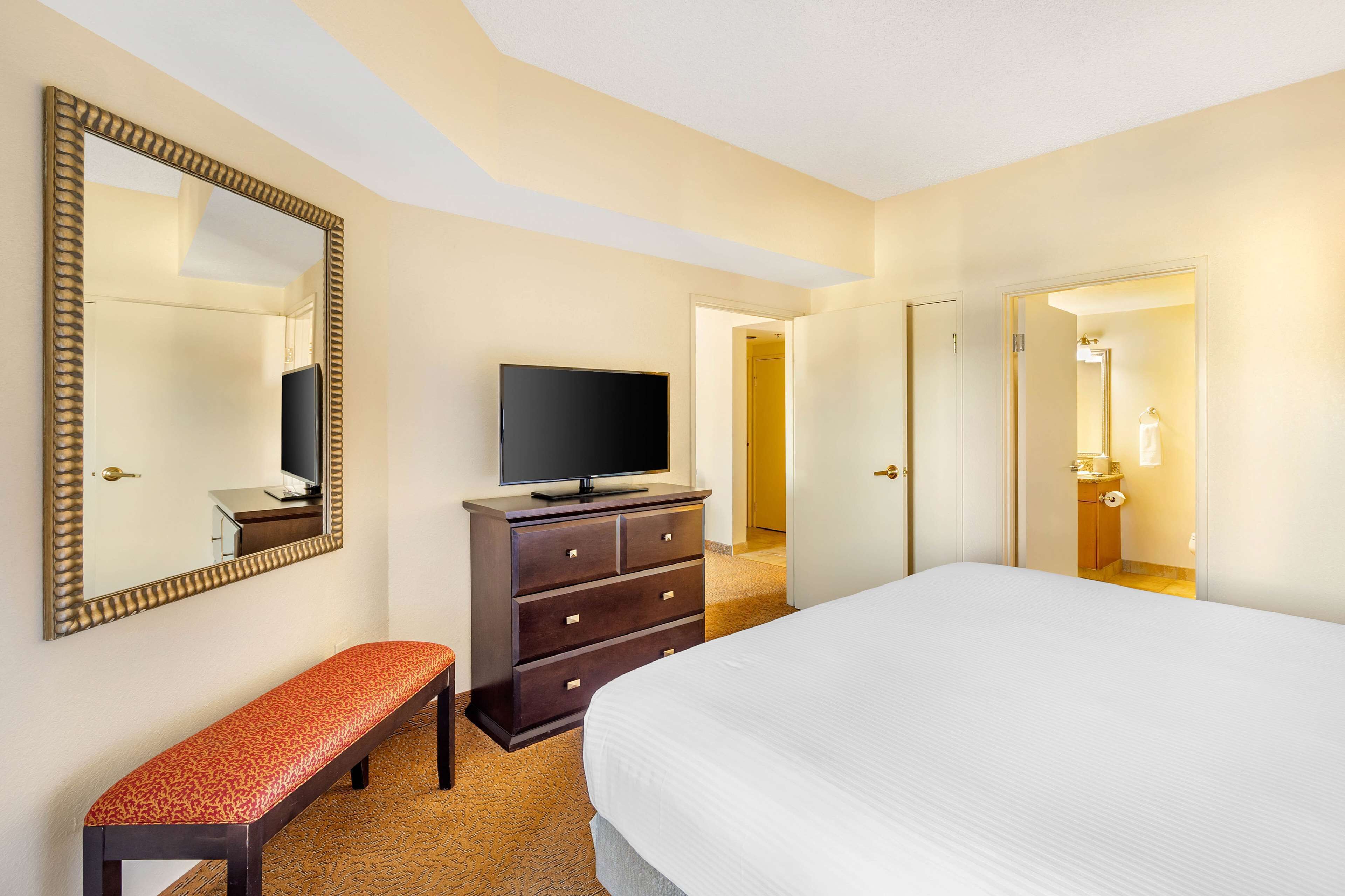 Habitación de hotel con una cama grande, un televisor en una cómoda, un banco y un espejo.