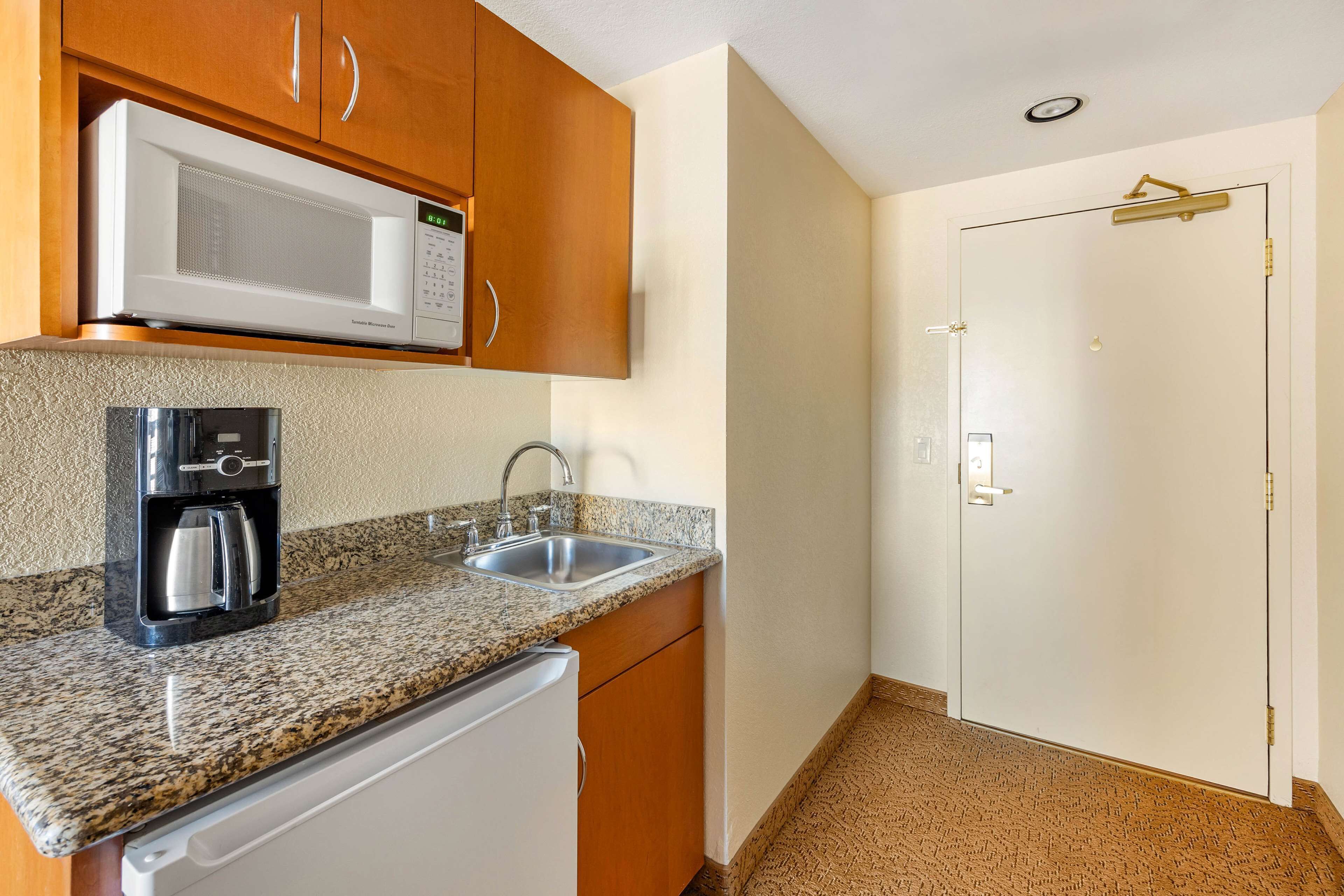 Una cocina compacta equipada con microondas, cafetera, pileta y refrigerador blanco.