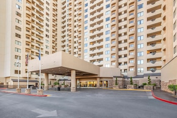 A hotel room with a large bed, a flat-screen TV, a balcony with a view of high-rise buildings, and a wooden headboard. at Hilton Vacation Club Polo Towers Las Vegas