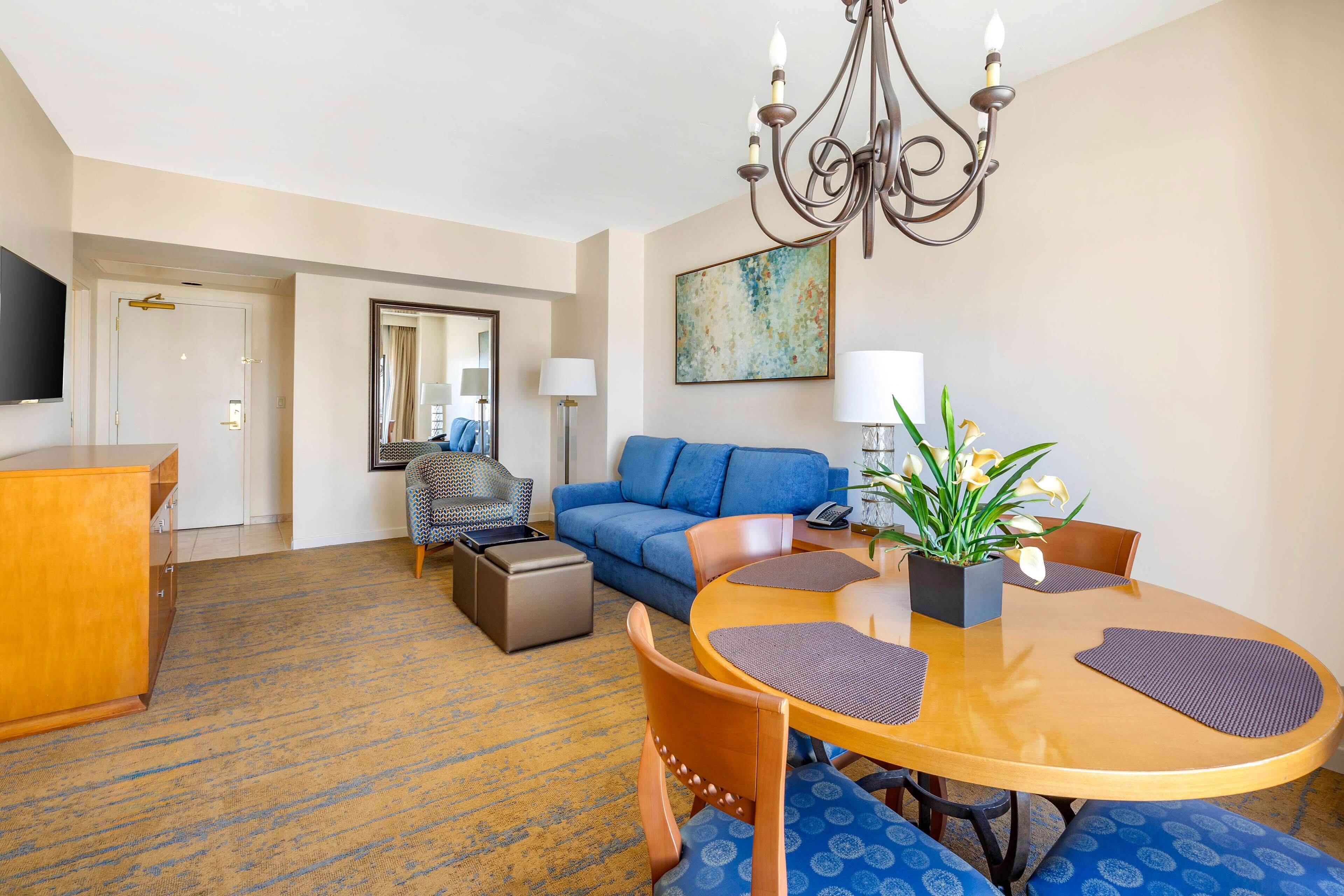 A hotel room with a dining area, a sofa, a television, and a chandelier.