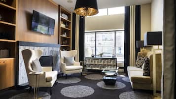 A modern living room with a large TV, comfortable seating, and a view of the city through large windows.
