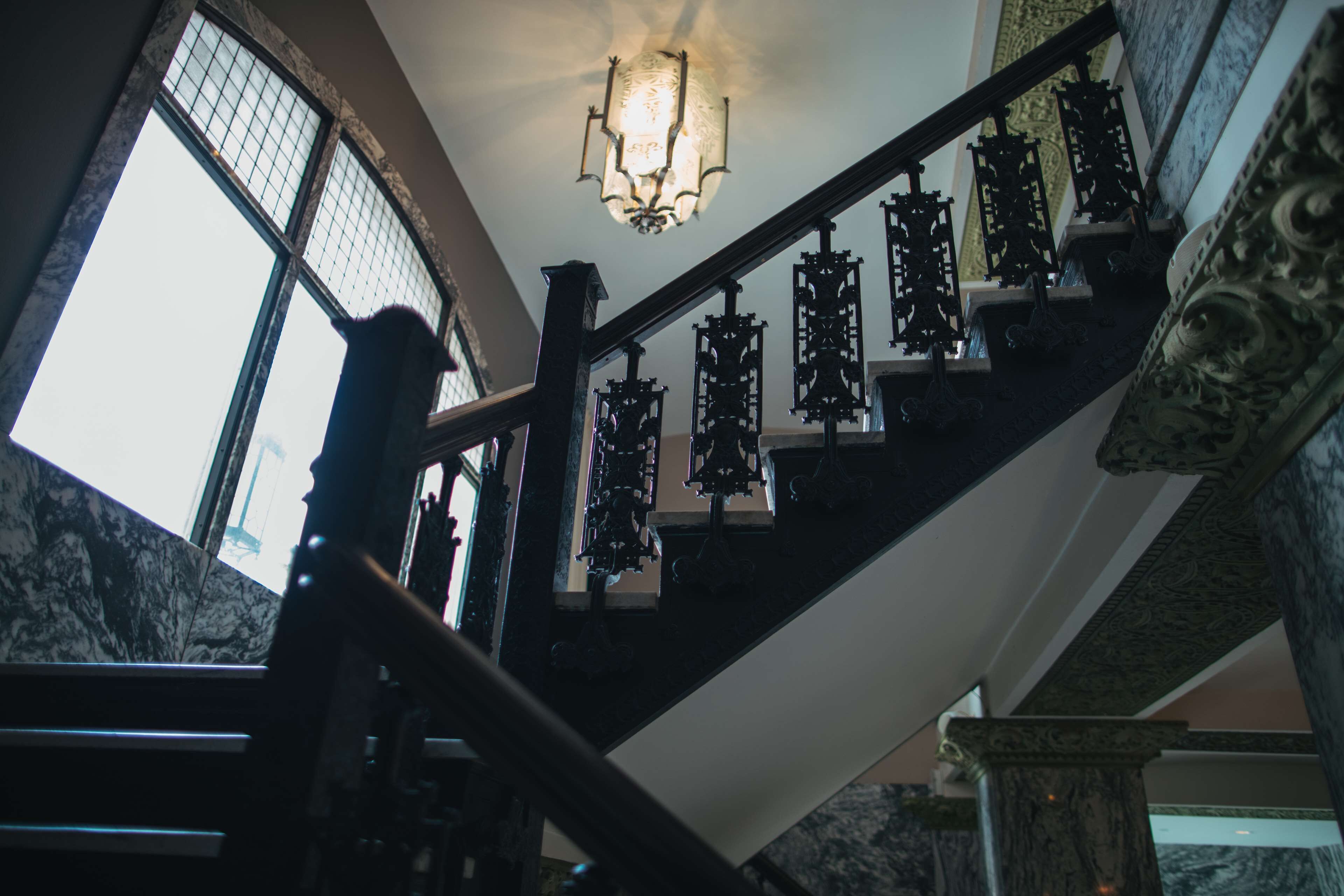 Una gran escalera con barandillas ornamentales y un candelabro, que conduce a un techo alto.