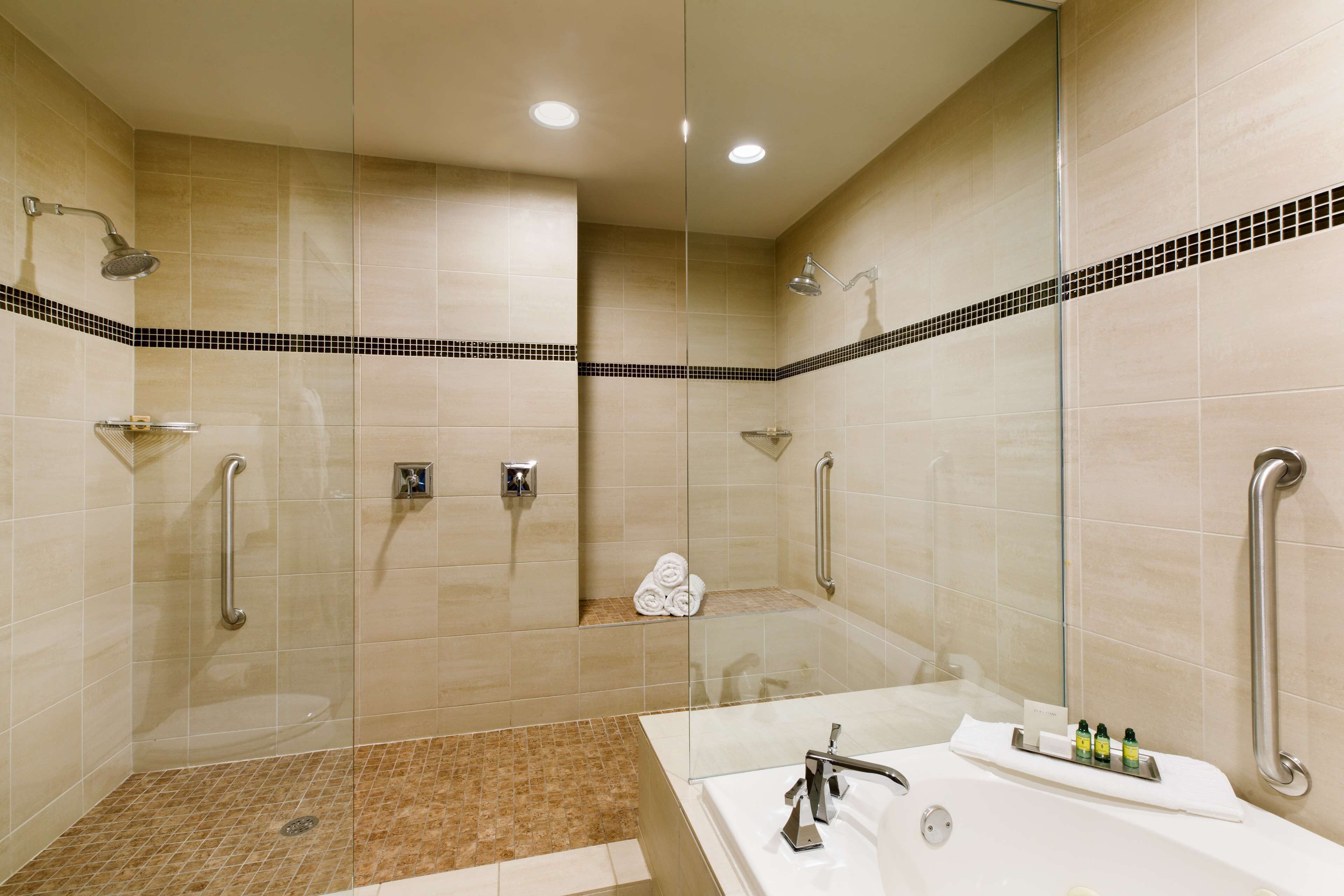 A modern bathroom with a glass-enclosed shower, a white bathtub, and a handrail.