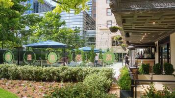 An outdoor seating area with umbrellas, potted plants, and a building with a modern facade in the background.