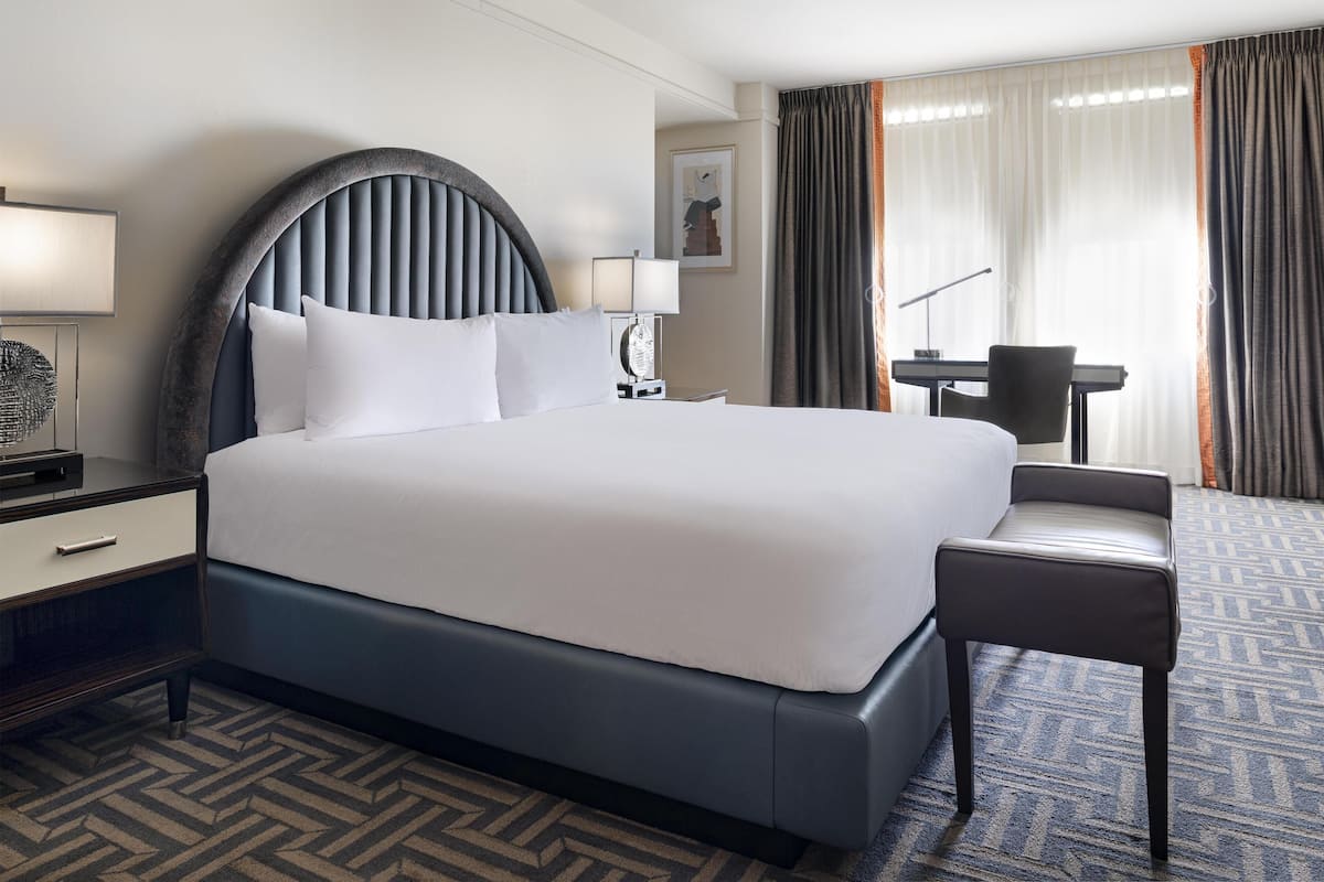 Una habitación de hotel con una cama grande, un escritorio, una silla y una lámpara.
