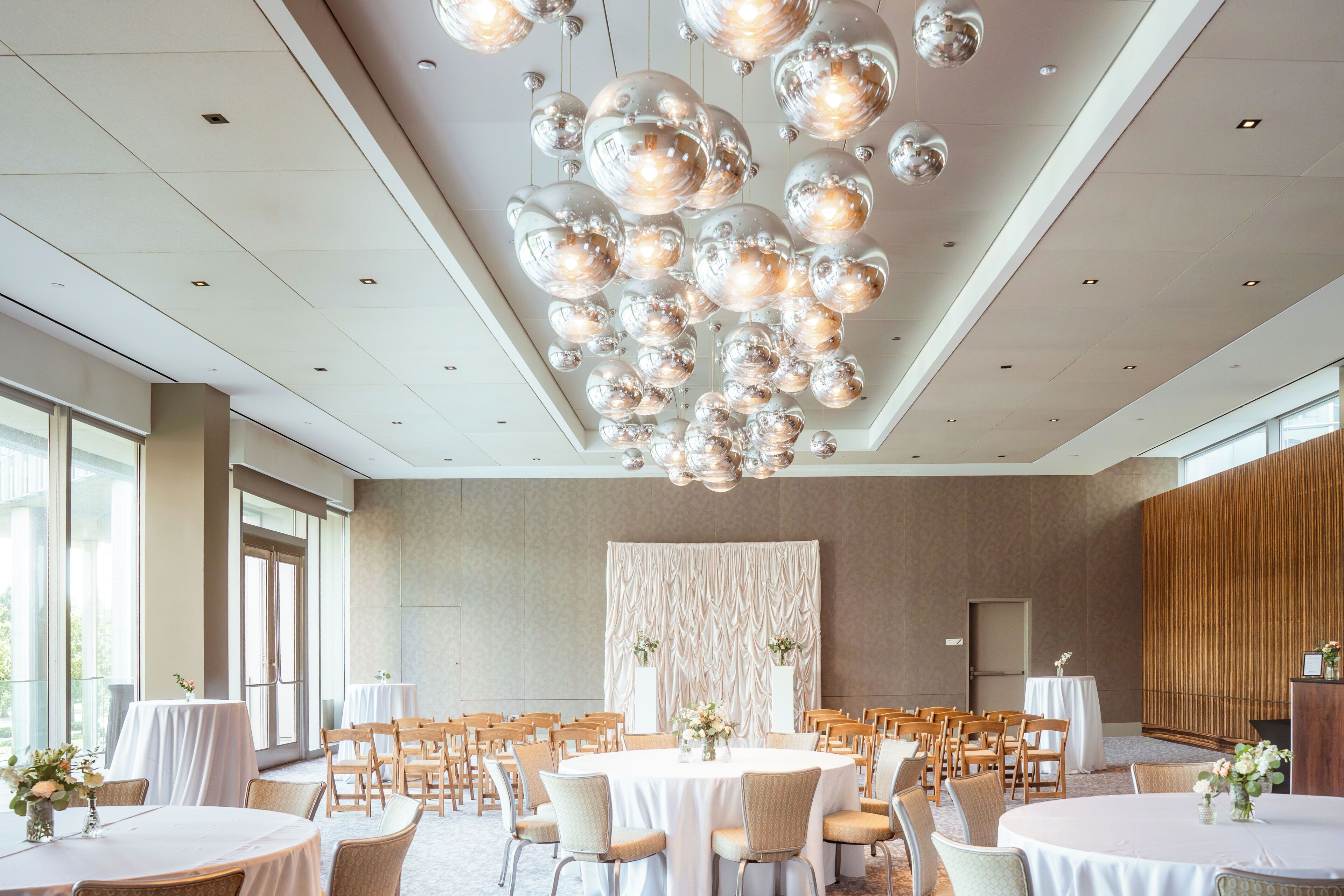 A spacious banquet hall with round tables, chairs, and a decorative ceiling with spherical light fixtures.