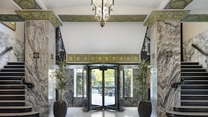 A grand lobby with marble columns, a central revolving door, and a chandelier. - Colcord Hotel Oklahoma City, Curio Collection by Hilton (Oklahoma City)