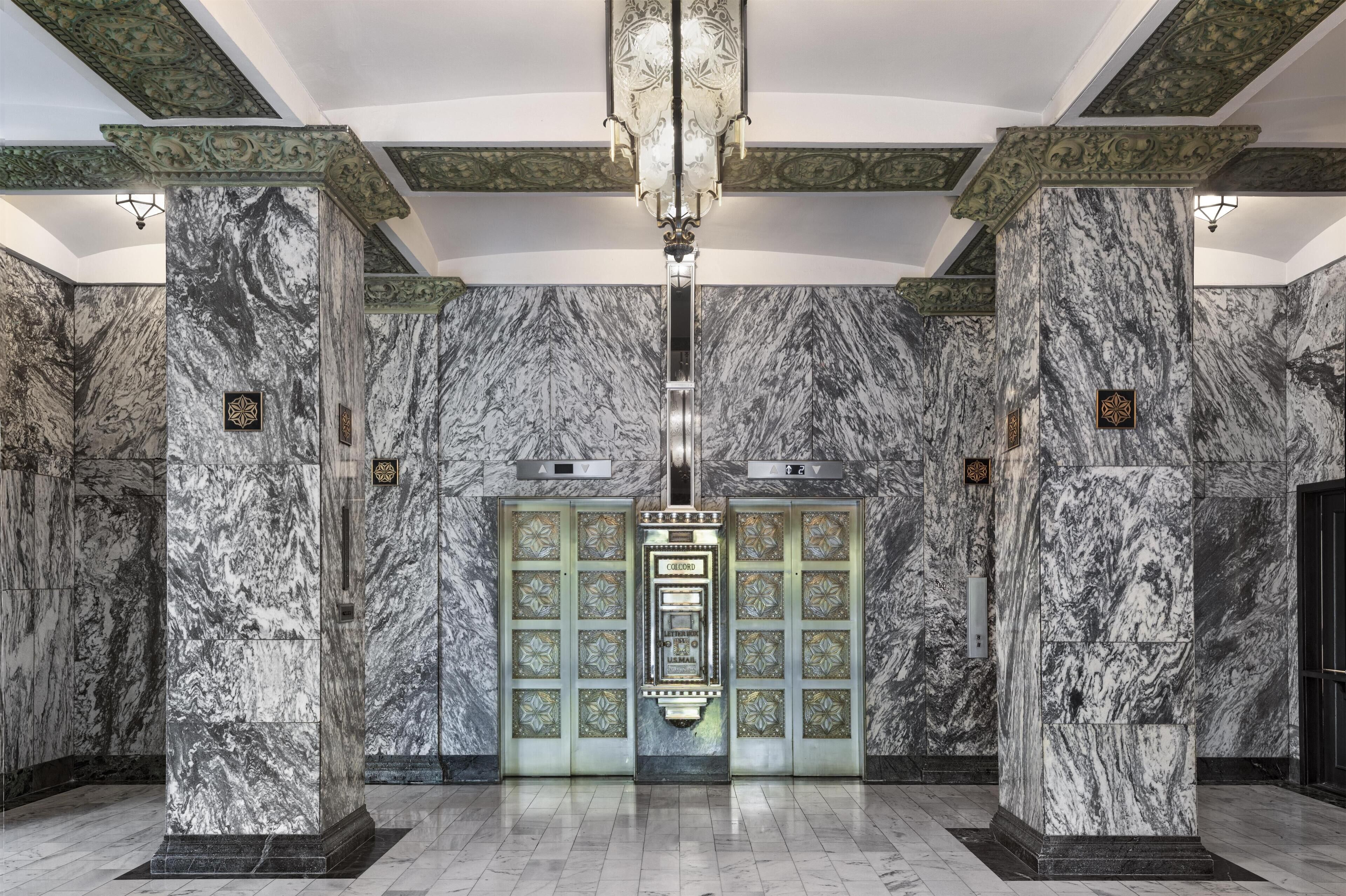 A lobby with marble walls, a central elevator, and decorative moldings.