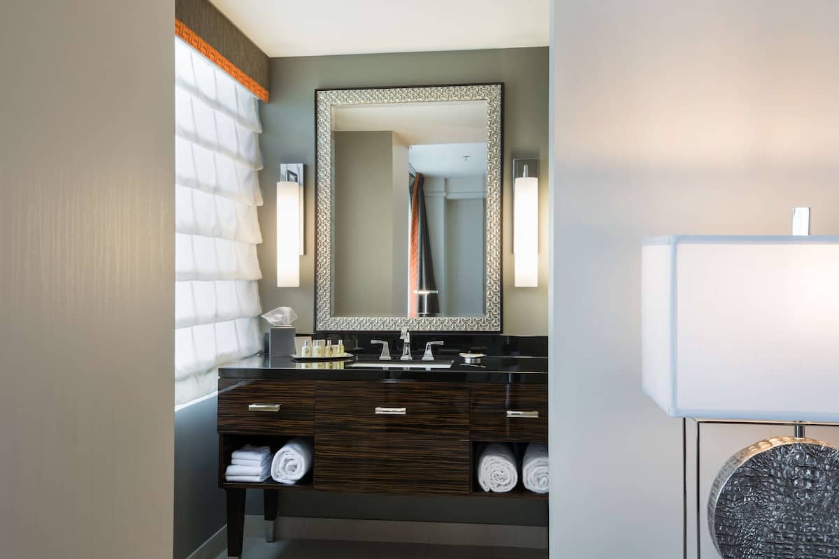Un baño moderno con tocador de madera oscura, un espejo grande y una lámpara redonda con textura.