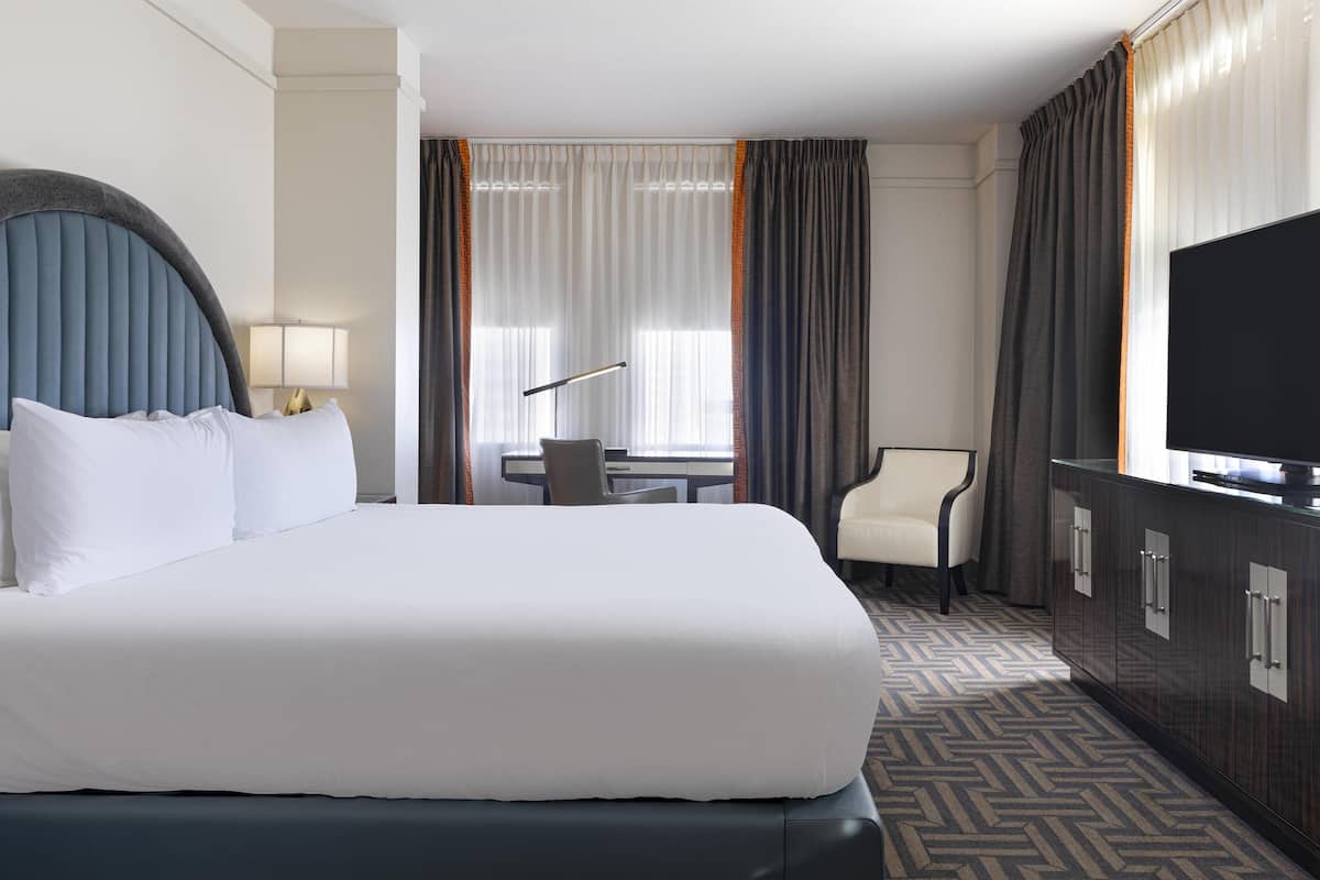 Una habitación de hotel con una cama grande, un escritorio, una silla, un televisor y un armario.