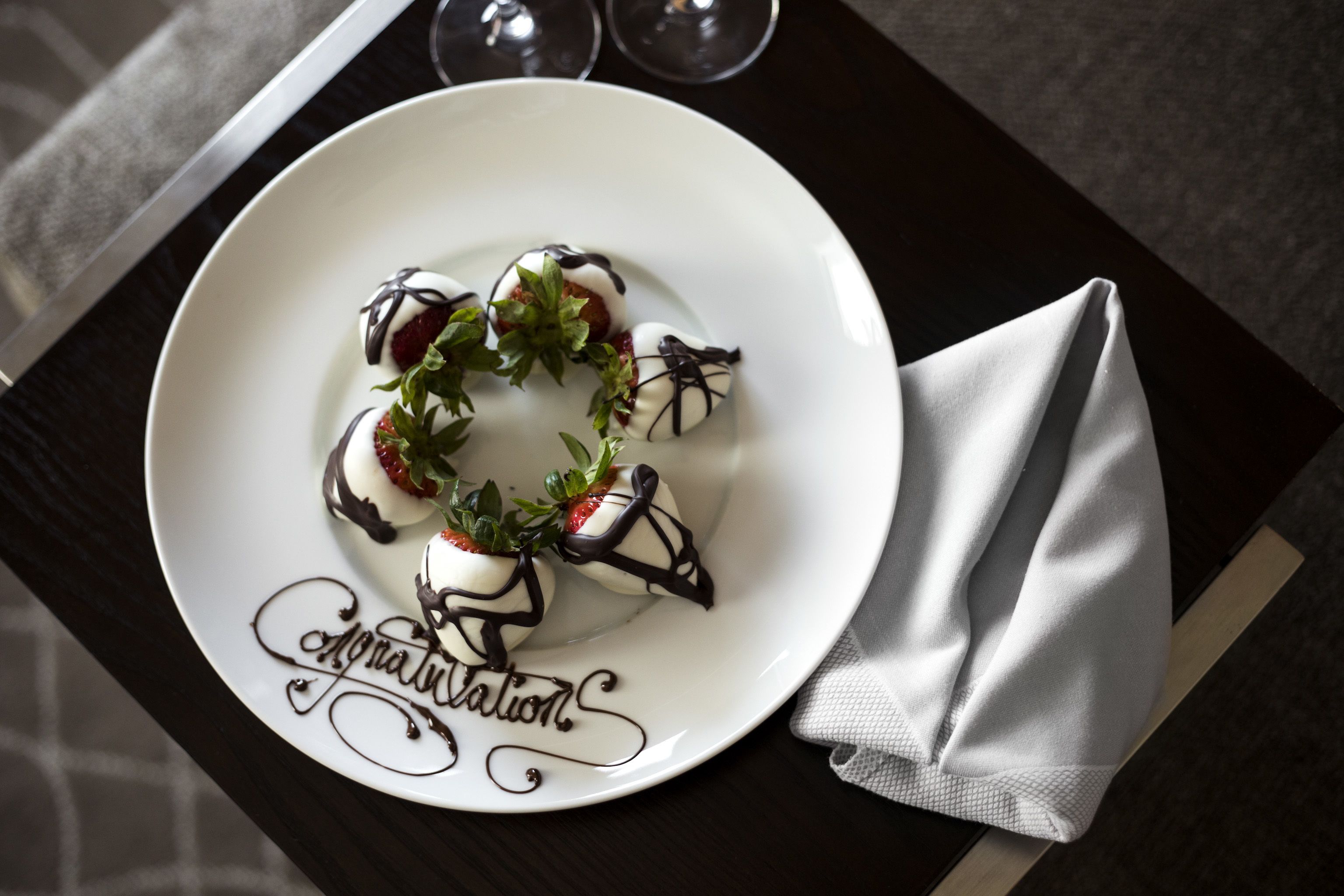 A white plate with chocolate-covered strawberries and a decorative chocolate drizzle, placed on a dark table with a white napkin.