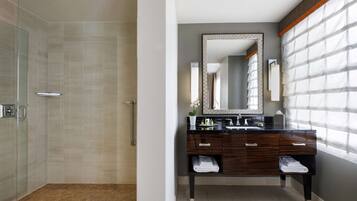 A modern bathroom with a glass-enclosed shower, a vanity with a large mirror, and a window with blinds.