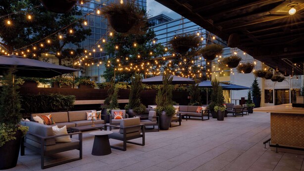 An outdoor seating area with multiple sofas and chairs, string lights, and hanging planters. - Colcord Hotel Oklahoma City, Curio Collection by Hilton (Oklahoma City)